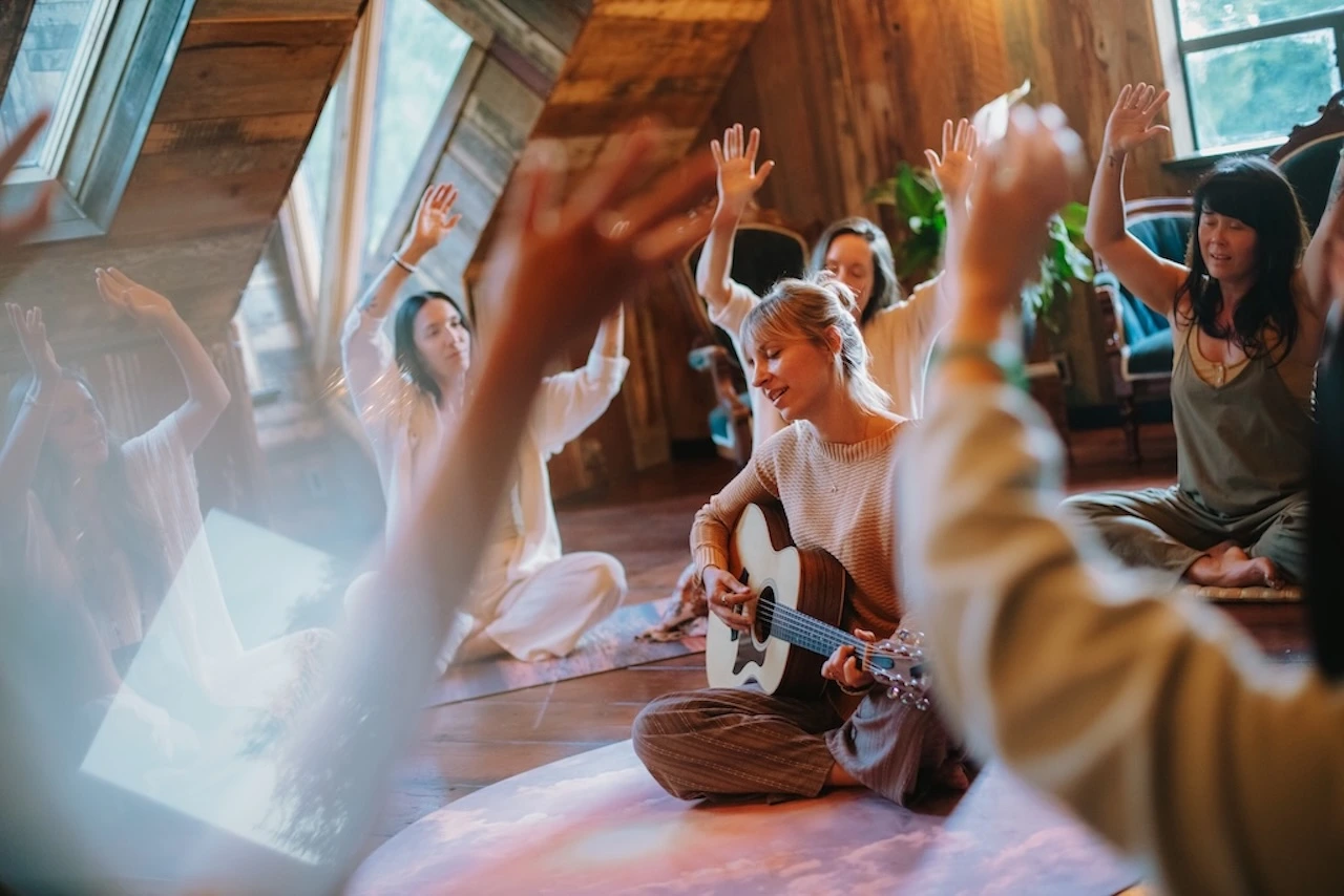 Tatiana playing guitar among women singing with raised arms at Akasha Farms